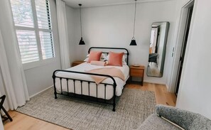 Une chambre à coucher avec un lit, des tables de chevet, un miroir et une fenêtre avec des stores.