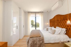 A bedroom with a large bed, a bench, a tufted headboard, and a view through a sliding door. - Penthouse at Aan de Meul (Stellenbosch)