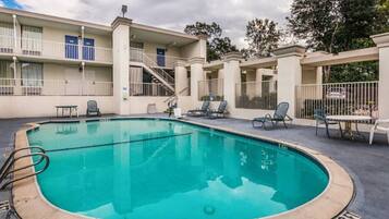 A swimming pool with a surrounding deck, lounge chairs, and a building with balconies.