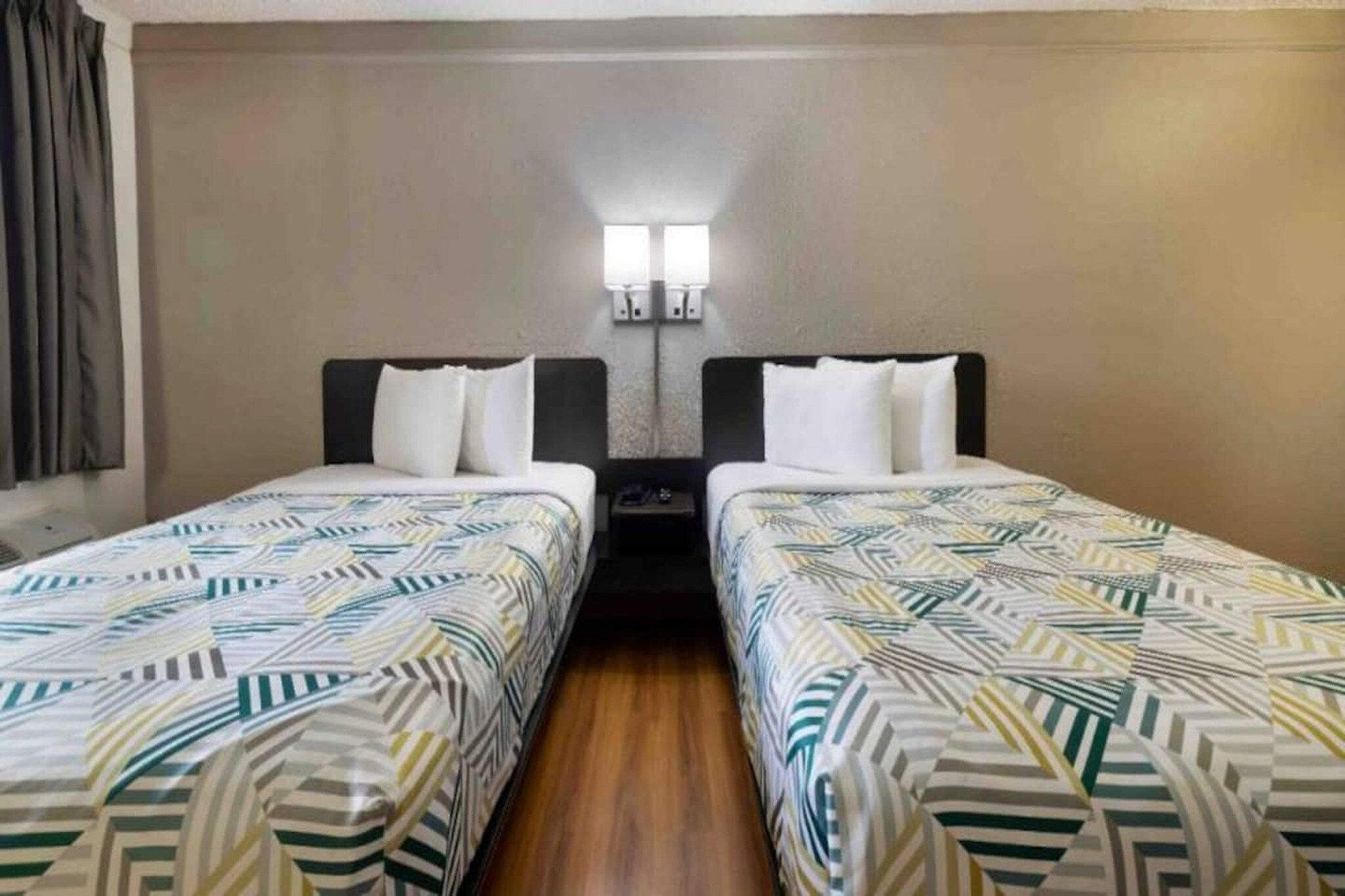 Een standaard hotelkamer met twee eenpersoonsbedden, een nachtkastje en een wandlamp.