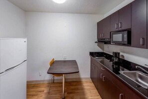 Una cocina compacta con un refrigerador blanco, un microondas, un lavabo y una pequeña mesa de comedor.