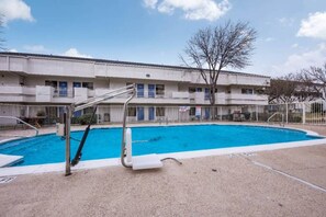 A swimming pool with a diving board, surrounded by a building with multiple balconies and a clear sky. - 2 FULL BEDS | NON-SMOKING, KITCHEN (Irving TX)