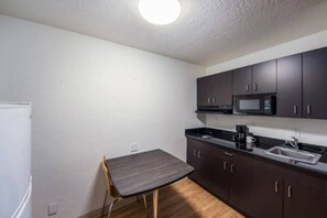 A compact kitchen with dark cabinets, a microwave, a sink, and a small table. - 2 FULL BEDS | NON-SMOKING, KITCHEN (Irving TX)