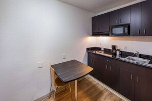 A compact kitchen with dark cabinets, a microwave, a coffee maker, and a small dining table. - 2 FULL BEDS | SMOKING, KITCHEN (Irving TX)