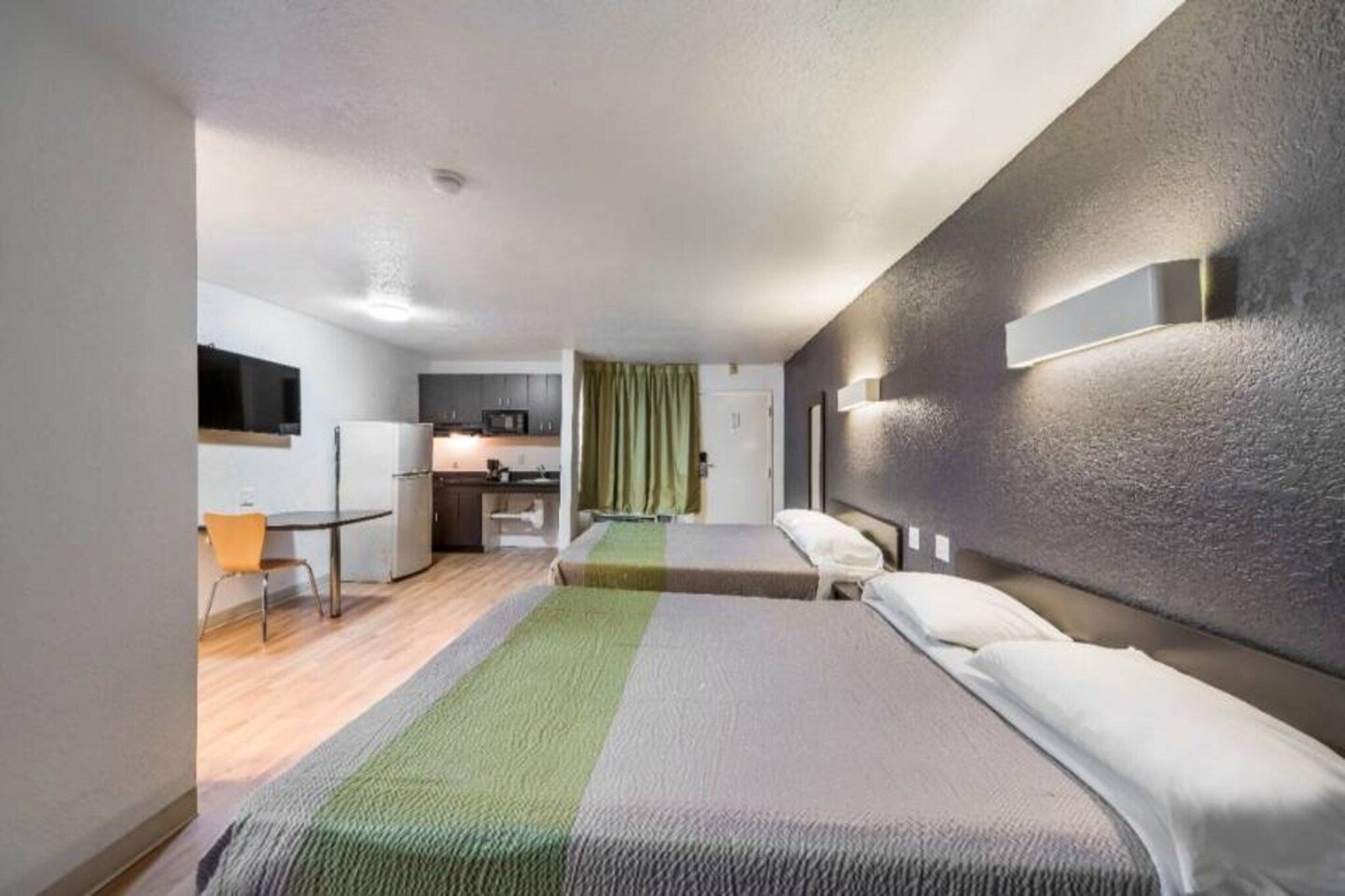 A hotel room with a bed, a desk, a chair, a microwave, and a small kitchenette.