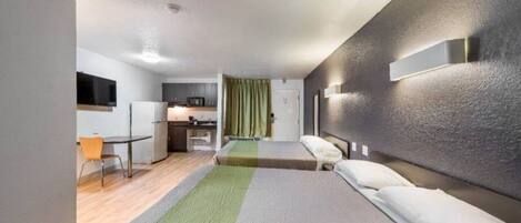 A hotel room with a bed, a desk, a chair, a microwave, and a small kitchenette.