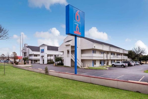 A motel with a large sign, multiple parking spaces, and a grassy area in front. - 2 FULL BEDS | SMOKING, KITCHEN (Irving TX)