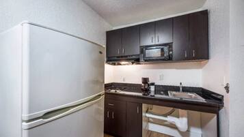 A compact kitchen with a refrigerator, microwave, and dark cabinets.