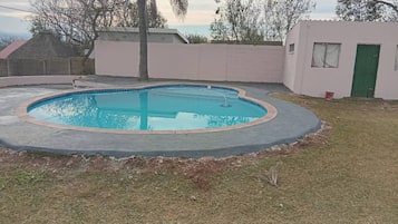 A swimming pool with a curved edge, surrounded by a concrete deck and a grassy area.