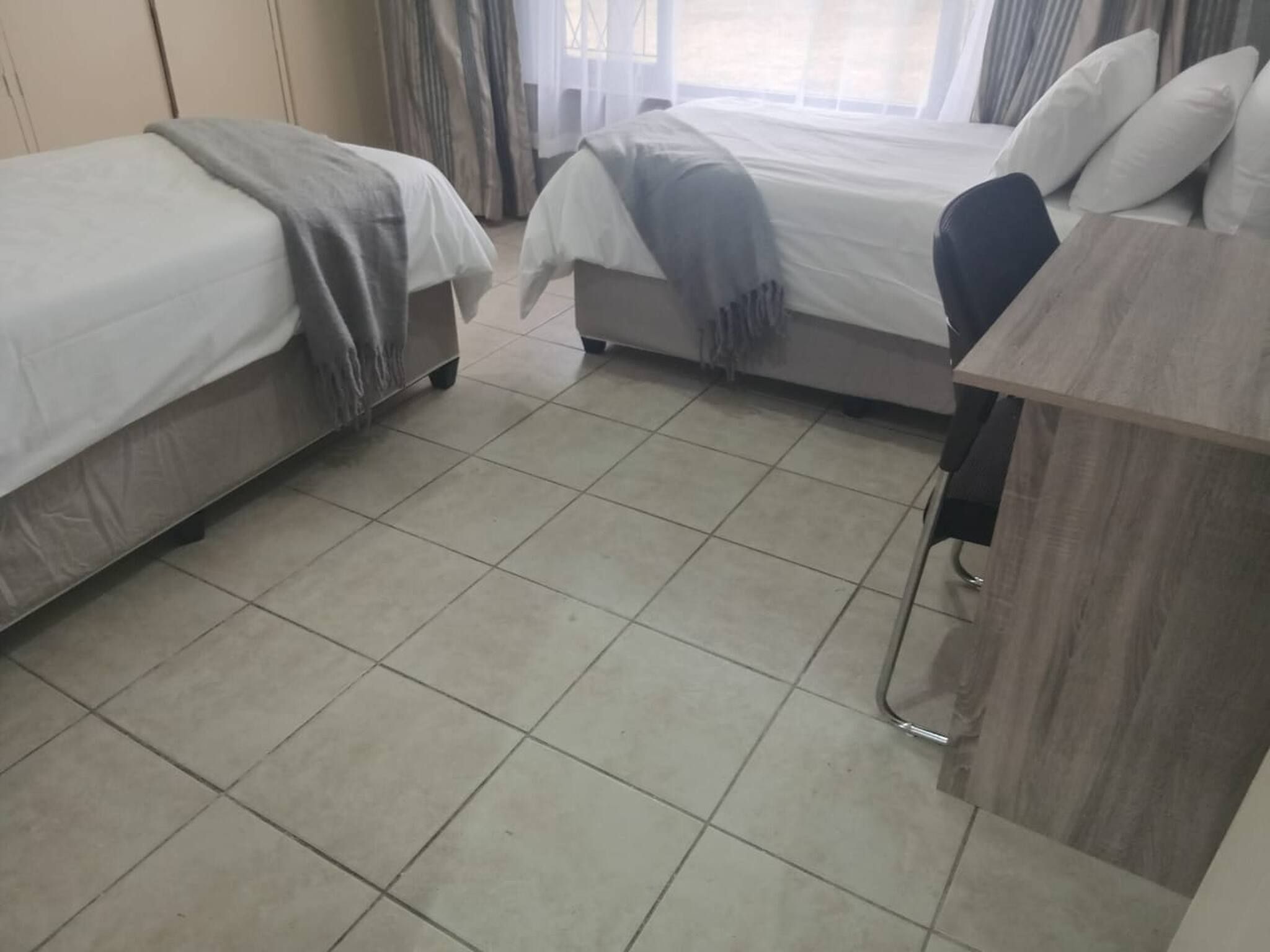 A hotel room with two beds, a wooden desk, and a tiled floor.