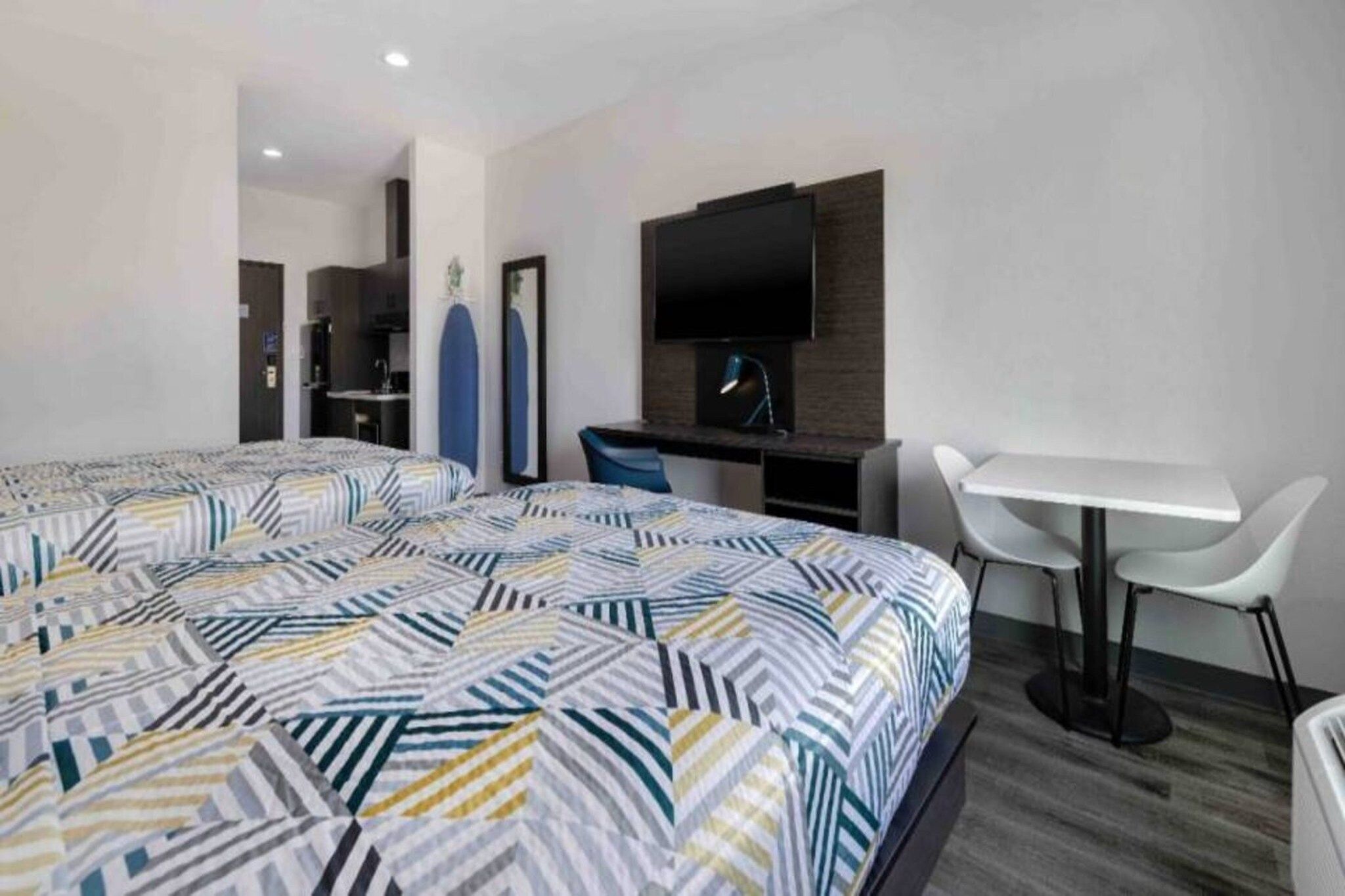 Una habitación de hotel con una cama grande, un escritorio, una silla, un televisor y una pequeña cocina.