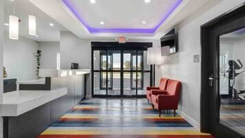 Zona de recepción con diseño moderno, que incluye un mostrador de recepción, un espacio de asientos con sillas rojas y un piso con rayas coloridas.