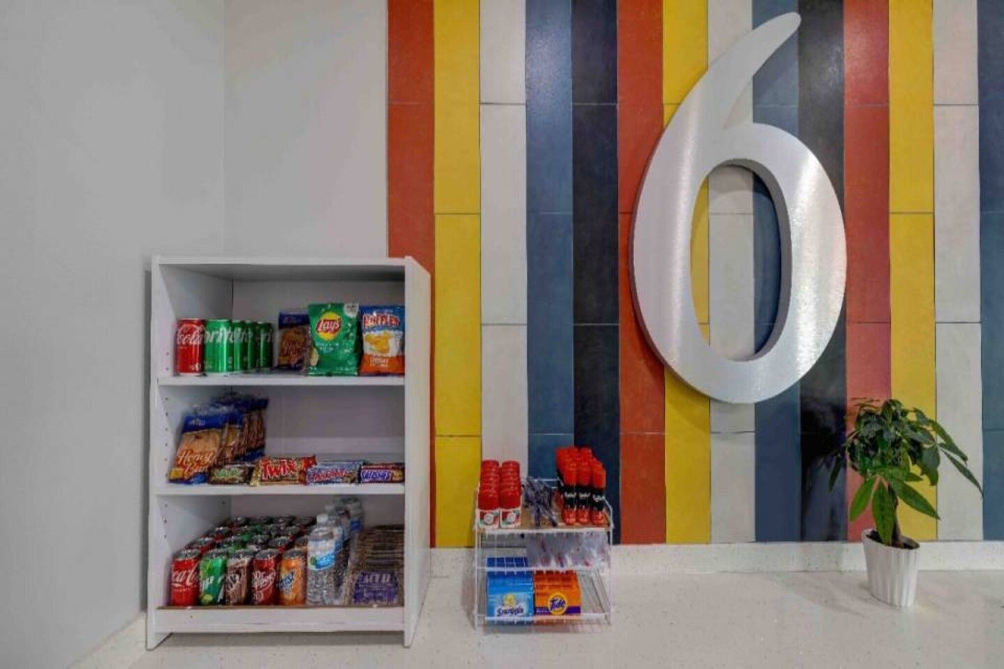 Máquina expendedora con aperitivos y bebidas, una decoración grande con el número 6 y una planta en maceta.