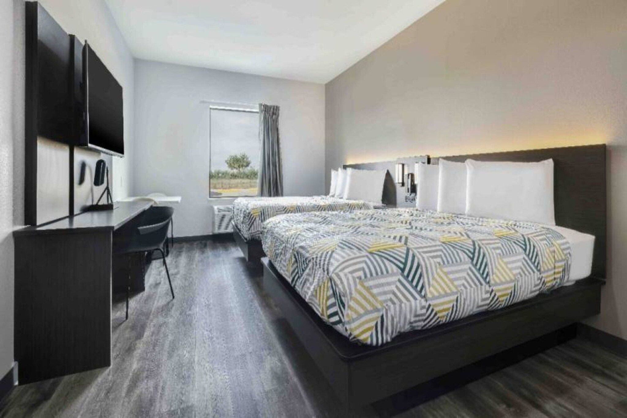 A hotel room with a large bed, a desk, a flat-screen TV, and a window with curtains.