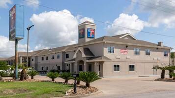 A multi-story building with a flat roof, a central entrance with a canopy, and multiple windows. There are palm trees in front of the building.