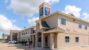 A multi-story hotel with a prominent Studio 6 sign, a covered entrance, and a parking lot with several vehicles.