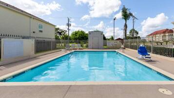 A rectangular pool with a tiled deck, surrounded by a metal fence, and a small utility shed in the background.
