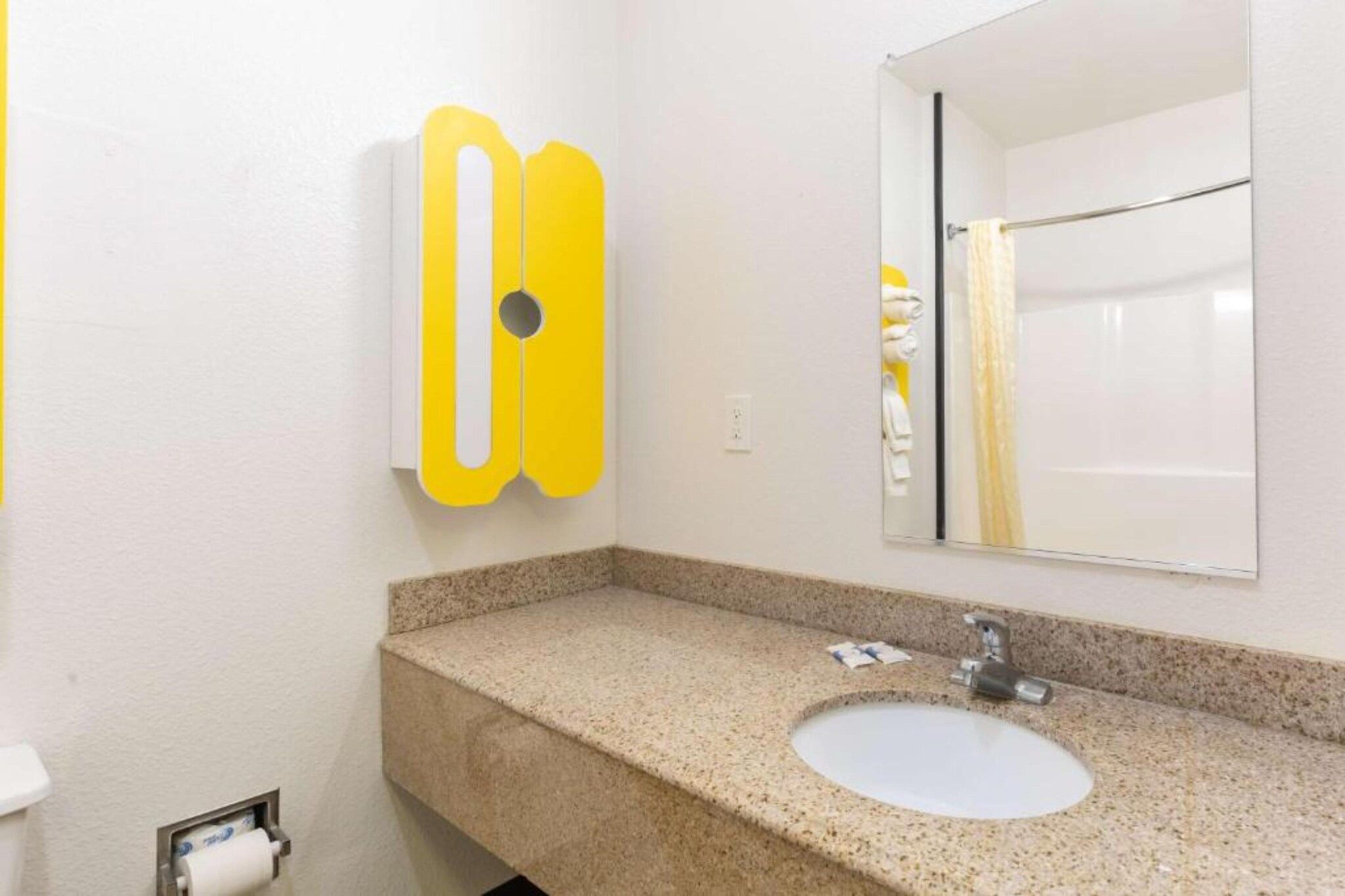 A bathroom with a granite countertop, a sink, a mirror, and a yellow soap dispenser.