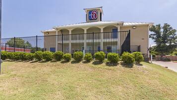 A Motel 6 building with a flat roof, a fenced parking area, and a well-maintained lawn.