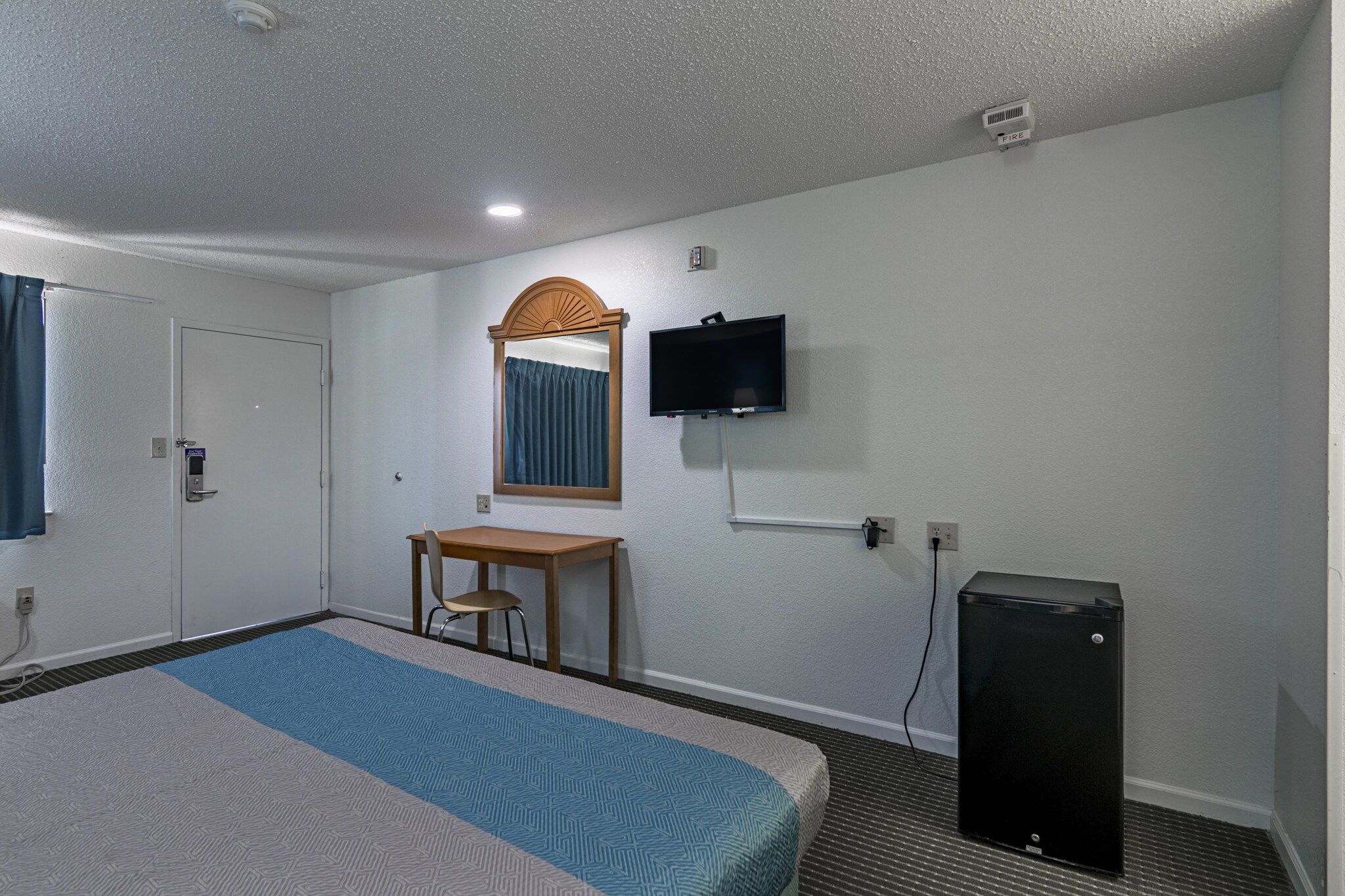 A hotel room with a bed, a desk, a chair, a television, and a small black speaker.