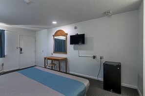 A hotel room with a bed, a desk, a chair, a television, and a small black speaker.