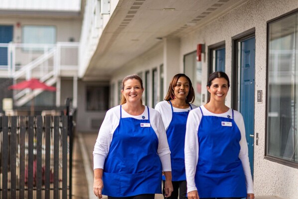 Three individuals in blue aprons walking outside a building with a staircase and a red umbrella in the background.