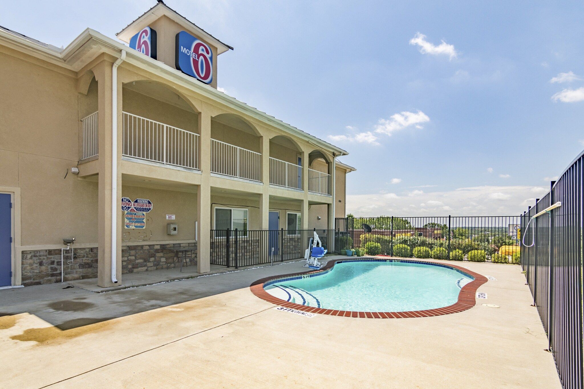 A motel with a swimming pool, a covered patio, and a sign indicating no lifeguard on duty.