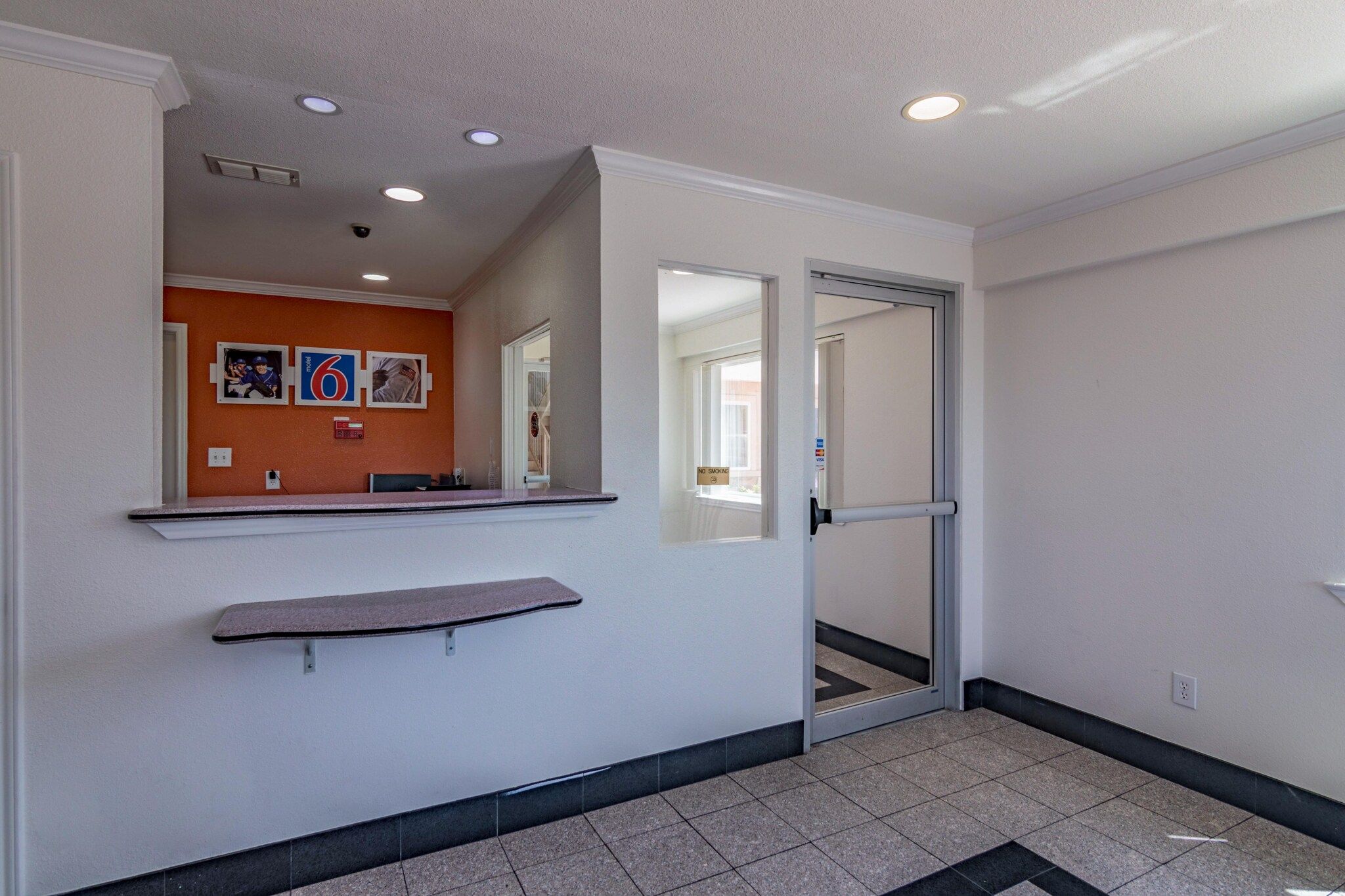 A hotel reception area with a counter, a no-smoking sign, and a door leading to another room.
