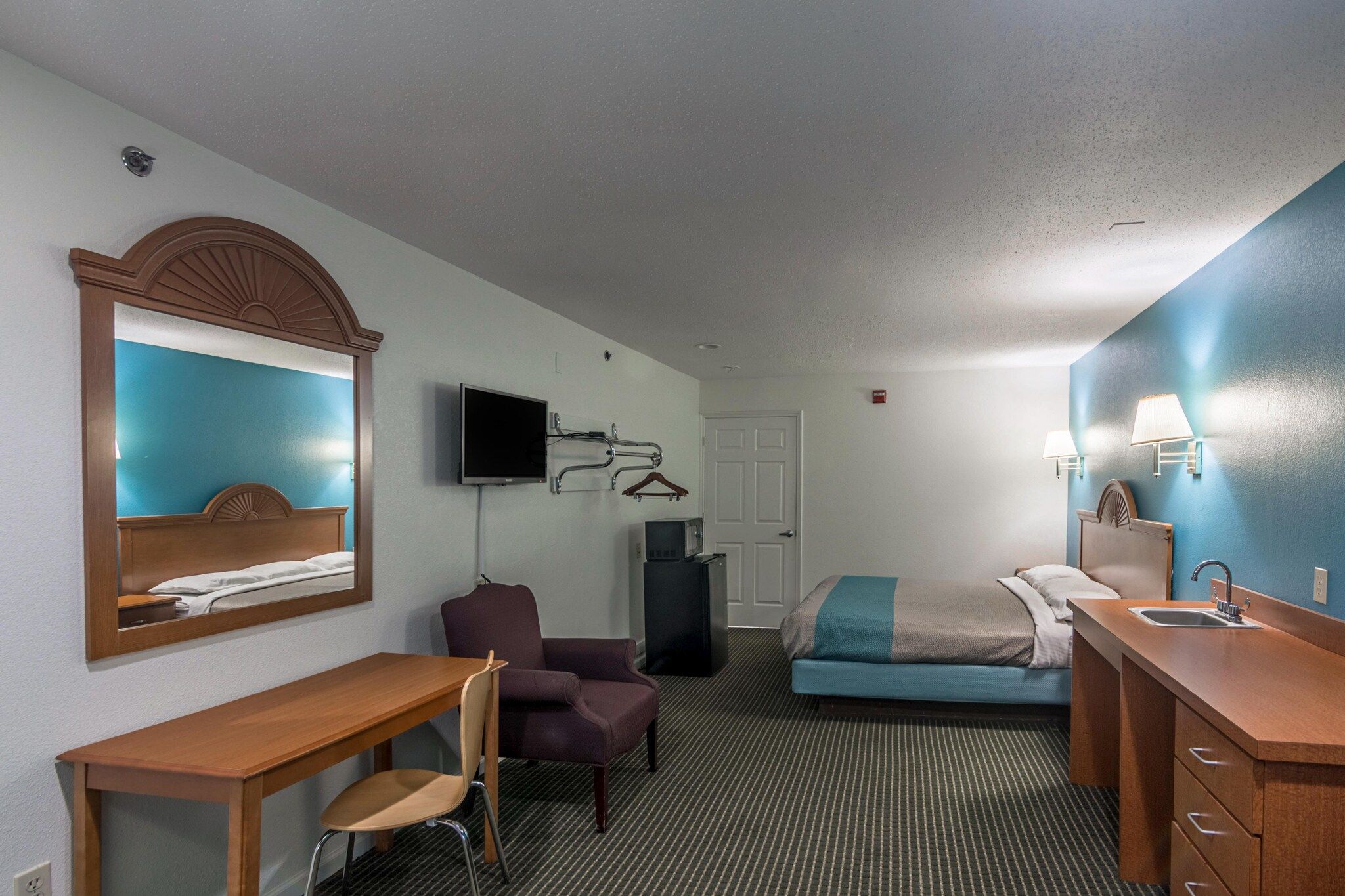 A hotel room with a bed, a desk, a chair, a television, a wardrobe, and a bathroom.