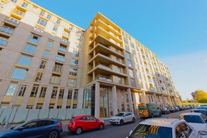 Ein mehrstöckiges Wohngebäude mit Backsteinfassade, mehreren Balkonen und einem Parkplatz mit verschiedenen Autos.