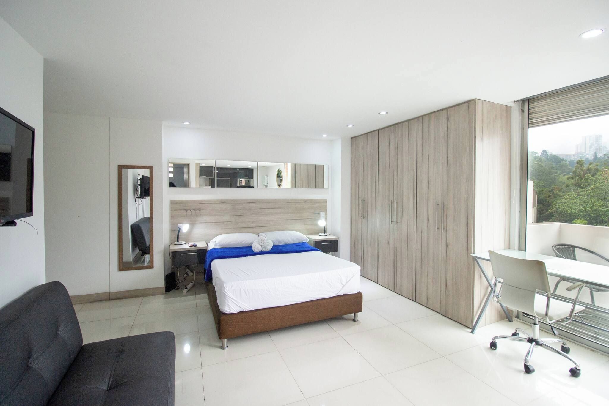 Une chambre d’hôtel moderne équipée d’un lit, d’un bureau, d’une chaise et d’une grande fenêtre.