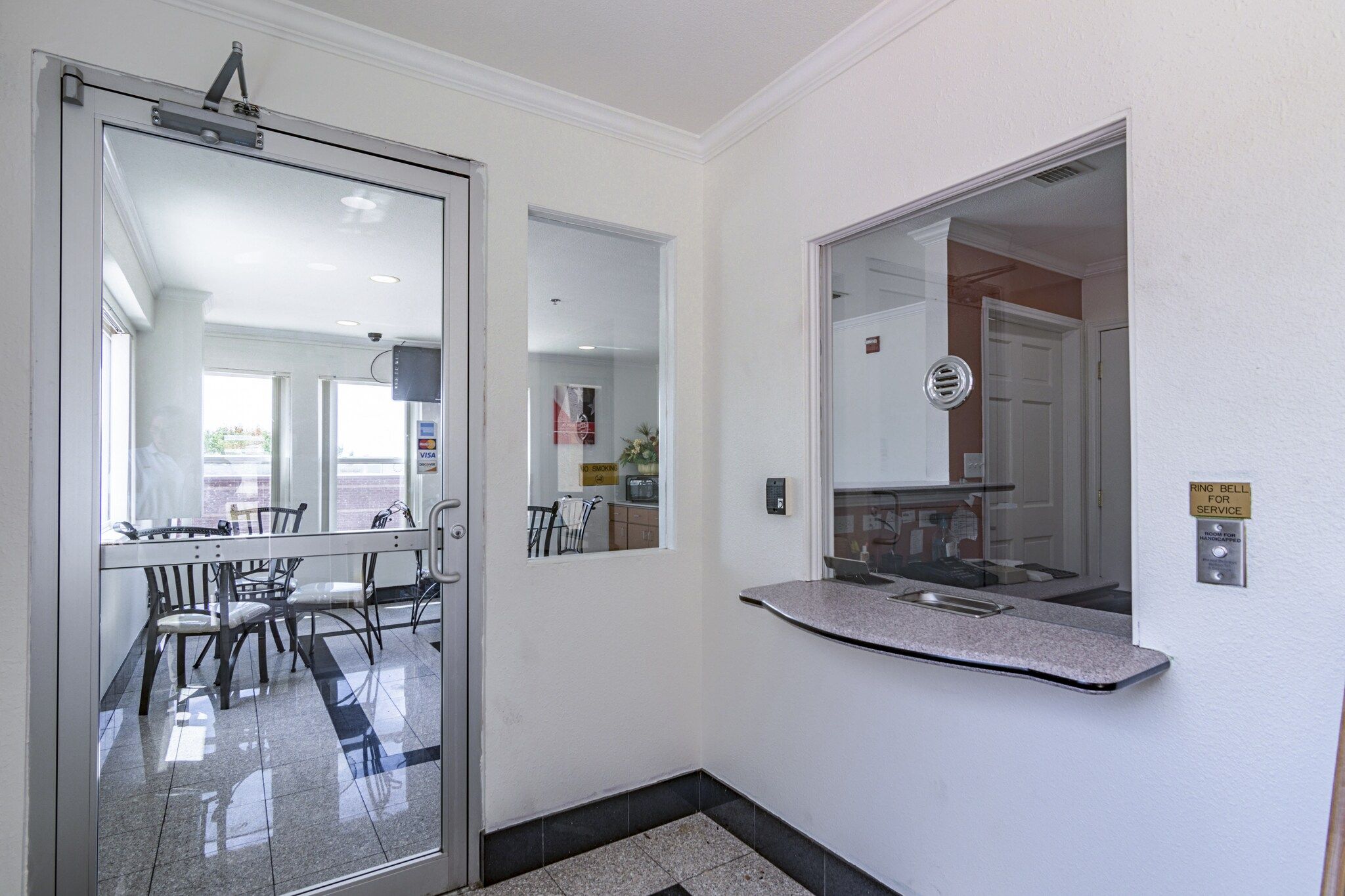 A hallway with a glass door leading to a dining area, a wall-mounted mirror, and a sign indicating a service bell.