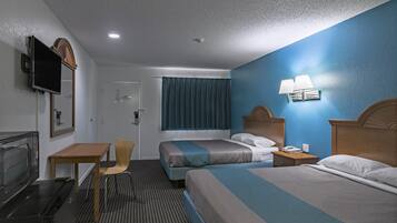 A hotel room with two beds, a desk, a chair, a television, and a window with curtains.
