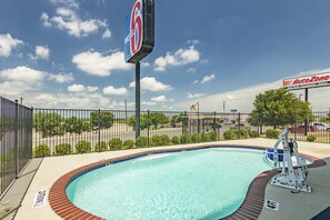A swimming pool with a fence, a sign for Motel 6, and an AutoZone store in the background.