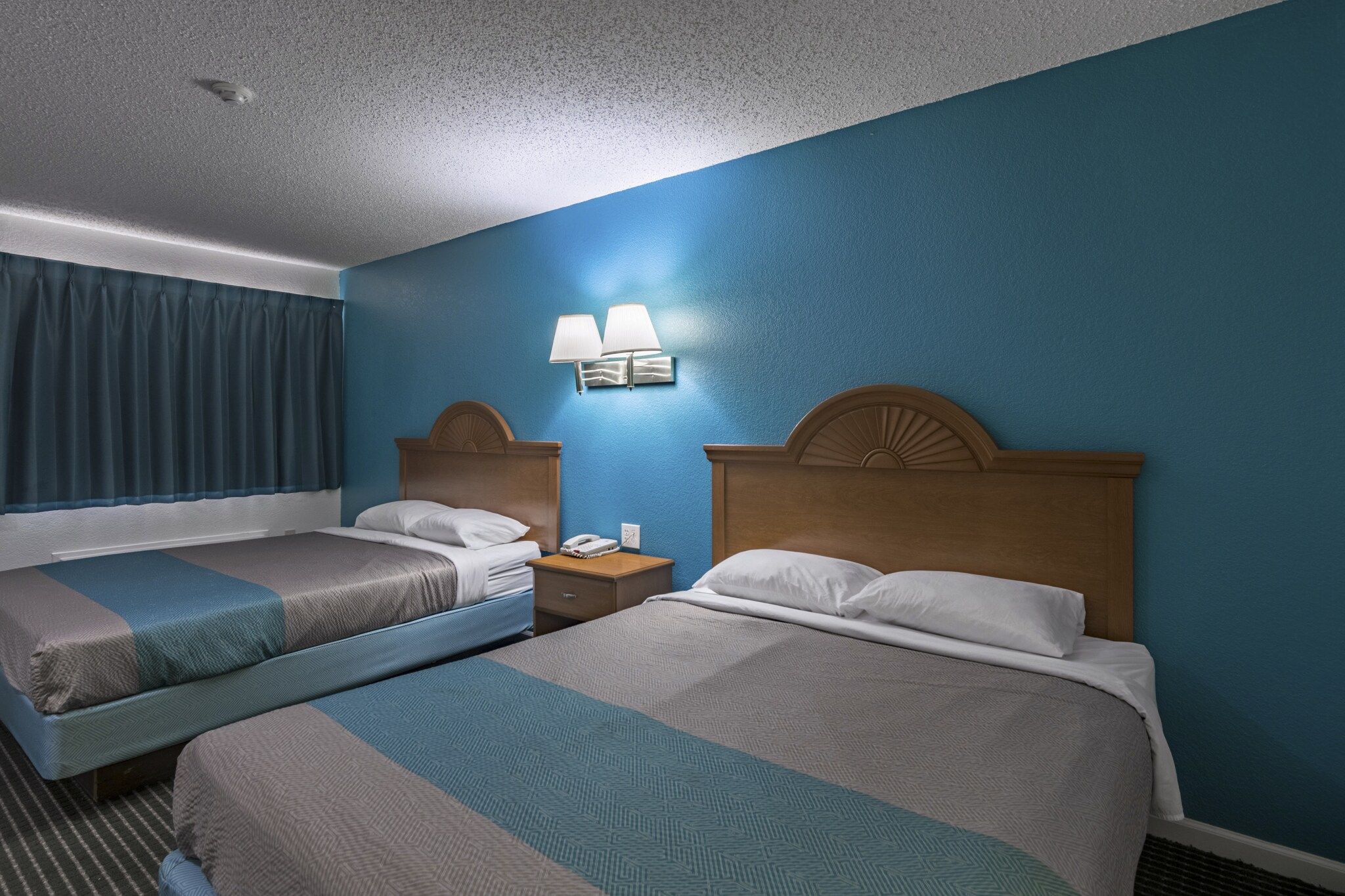 Ein Hotelzimmer mit zwei Betten, einem Nachttisch, einem Telefon und einer Wandlampe.