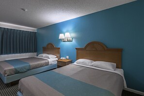 A hotel room with two beds, a nightstand, a telephone, and a wall-mounted lamp.