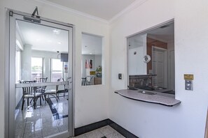A hallway with a glass door leading to a dining area, a wall-mounted mirror, and a sign indicating a service bell.