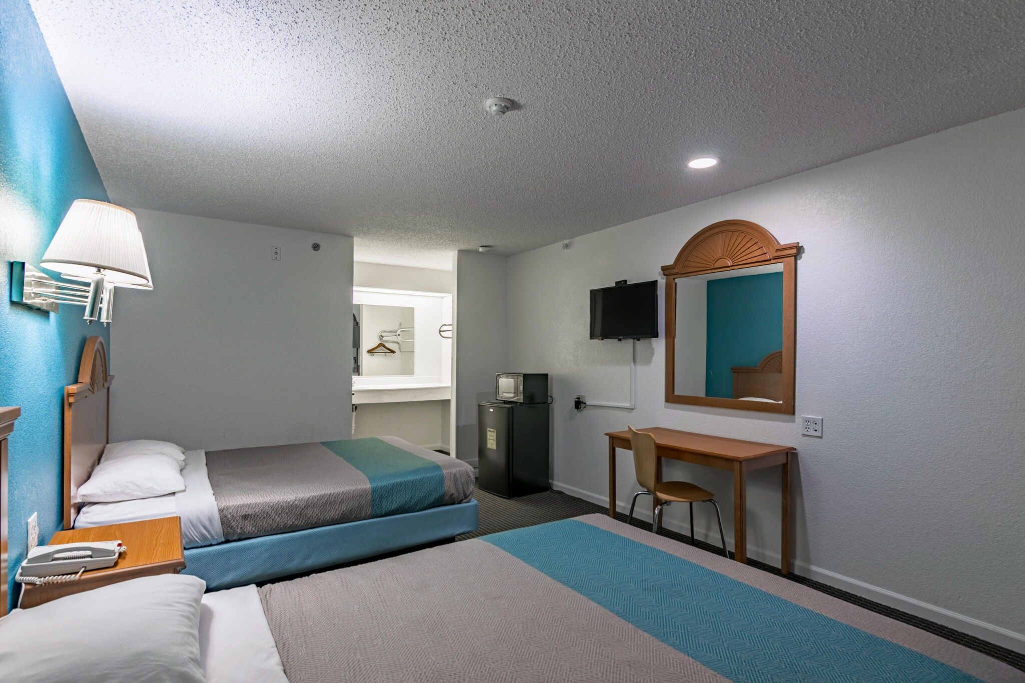 A hotel room with two beds, a desk, a chair, a television, and a mirror.