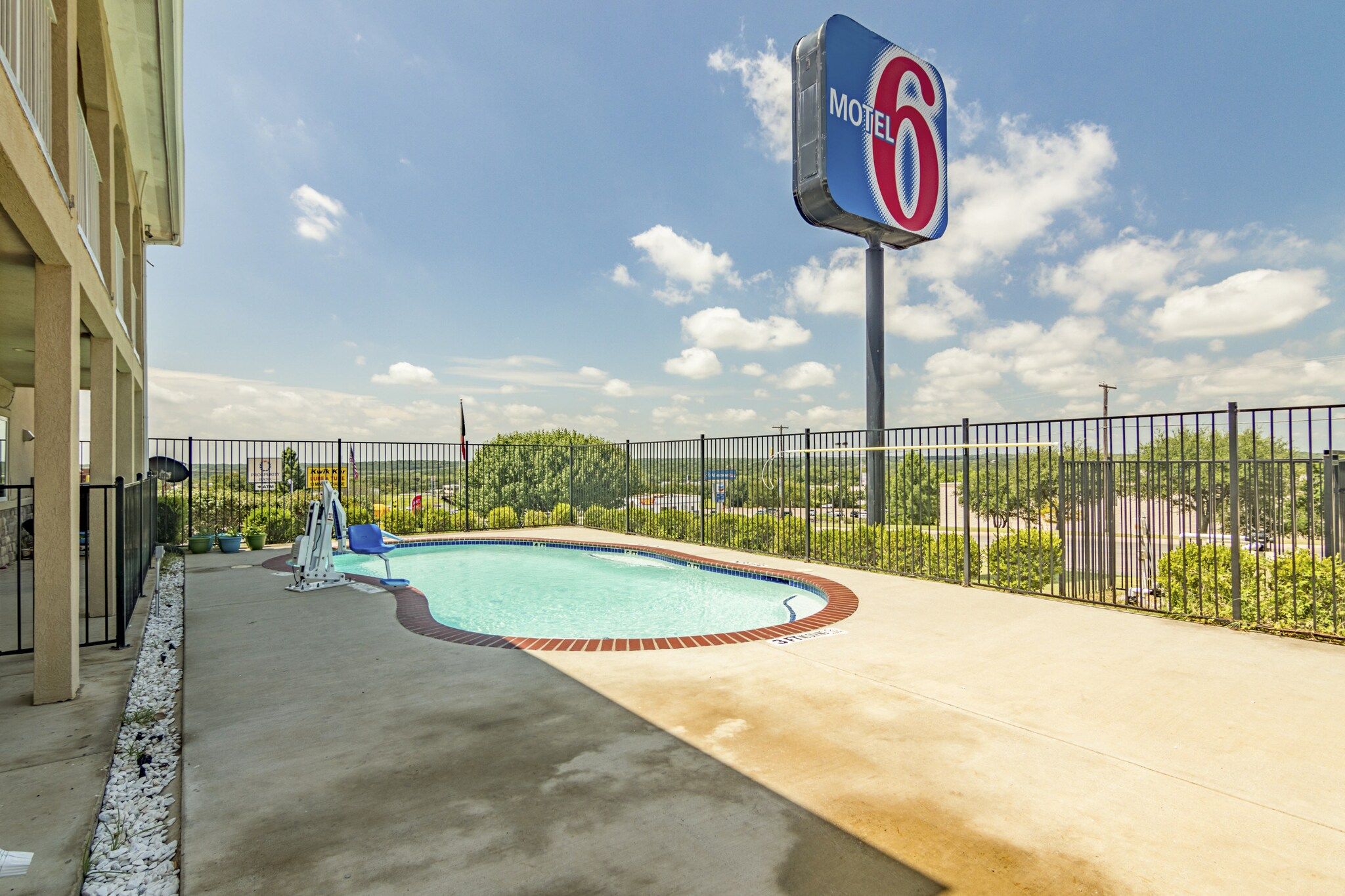 Ein Motel mit Schwimmbad, umzäunter Fläche und blauem Himmel.
