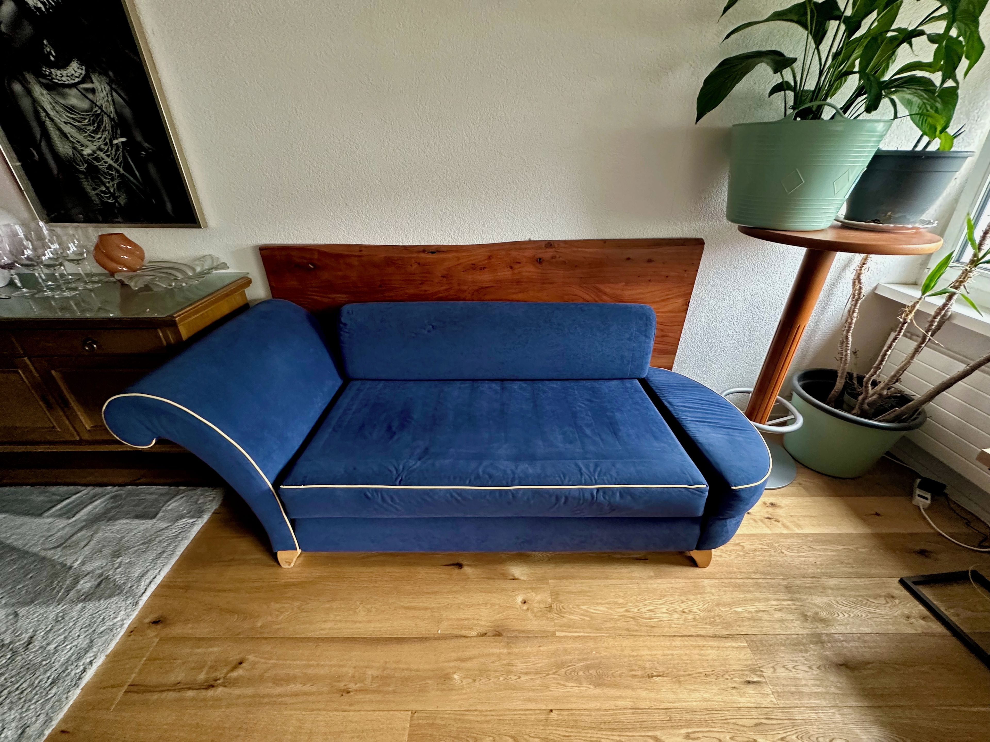 A blue sofa with a wooden headboard in a room with wooden flooring.