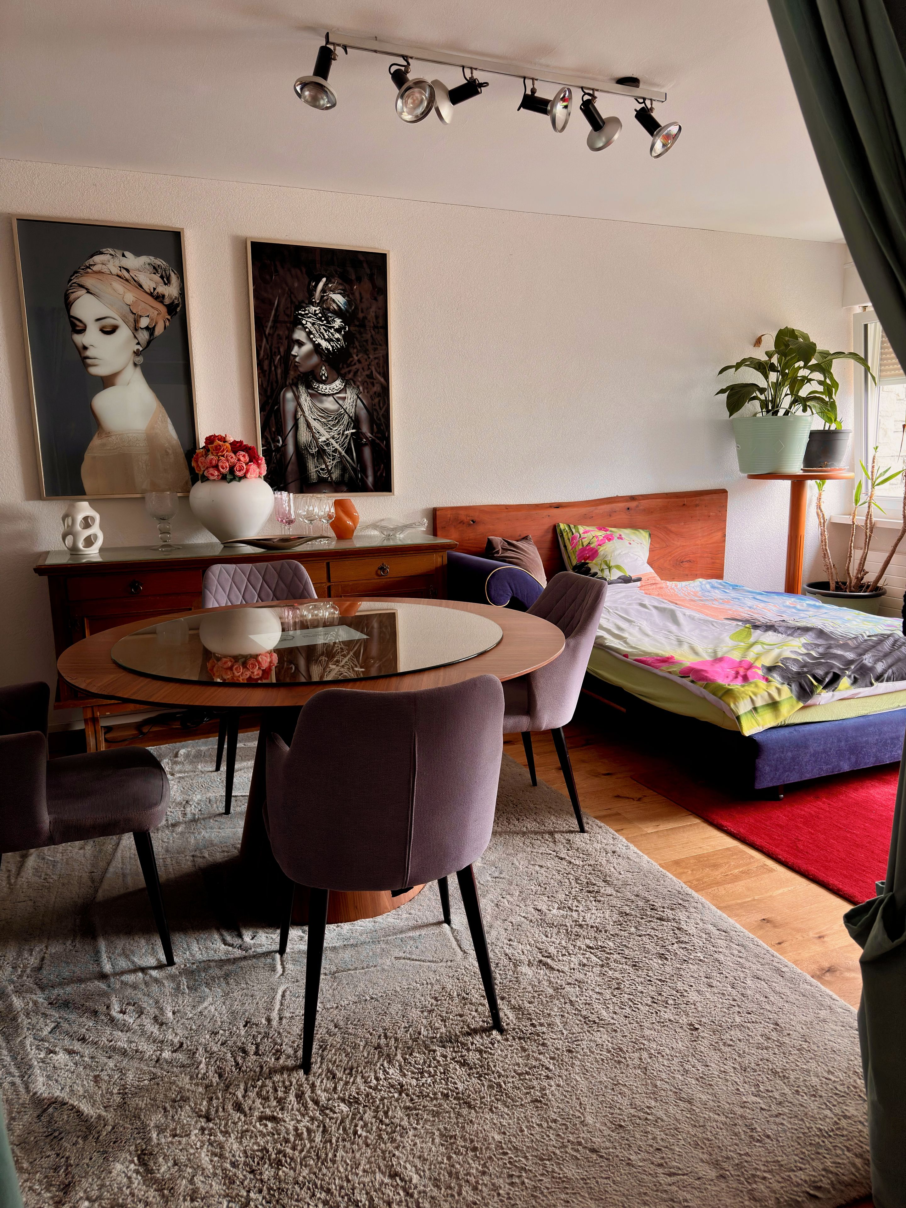 Un dormitorio moderno con cama, mesa de comedor, sillas, cómoda y obras de arte en las paredes.