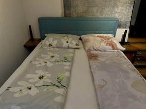A bed with floral bedding, a teal headboard, and a bedside table with a lamp.