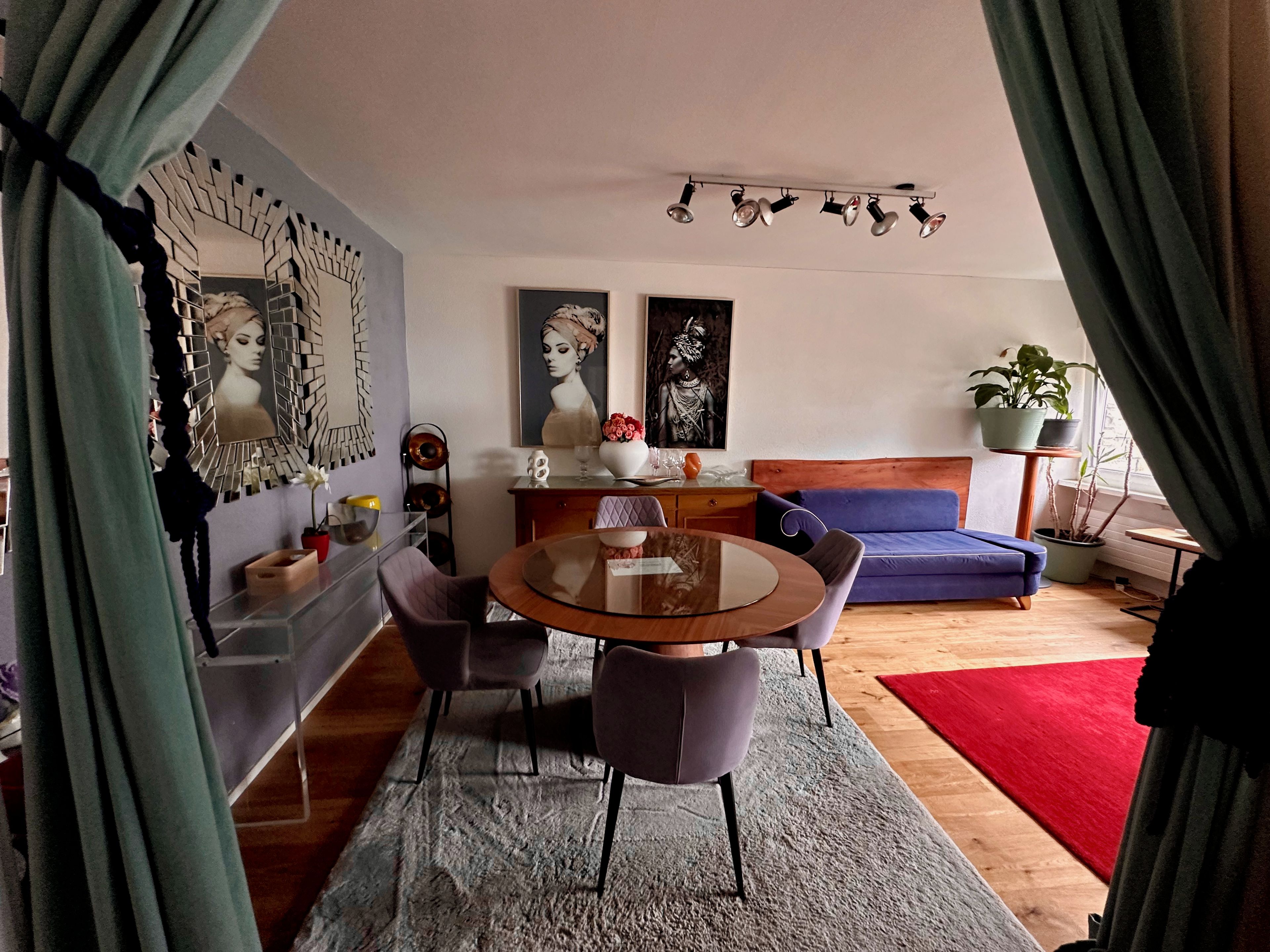 A modern living room with a round glass table, purple chairs, a blue sofa, and a red rug.