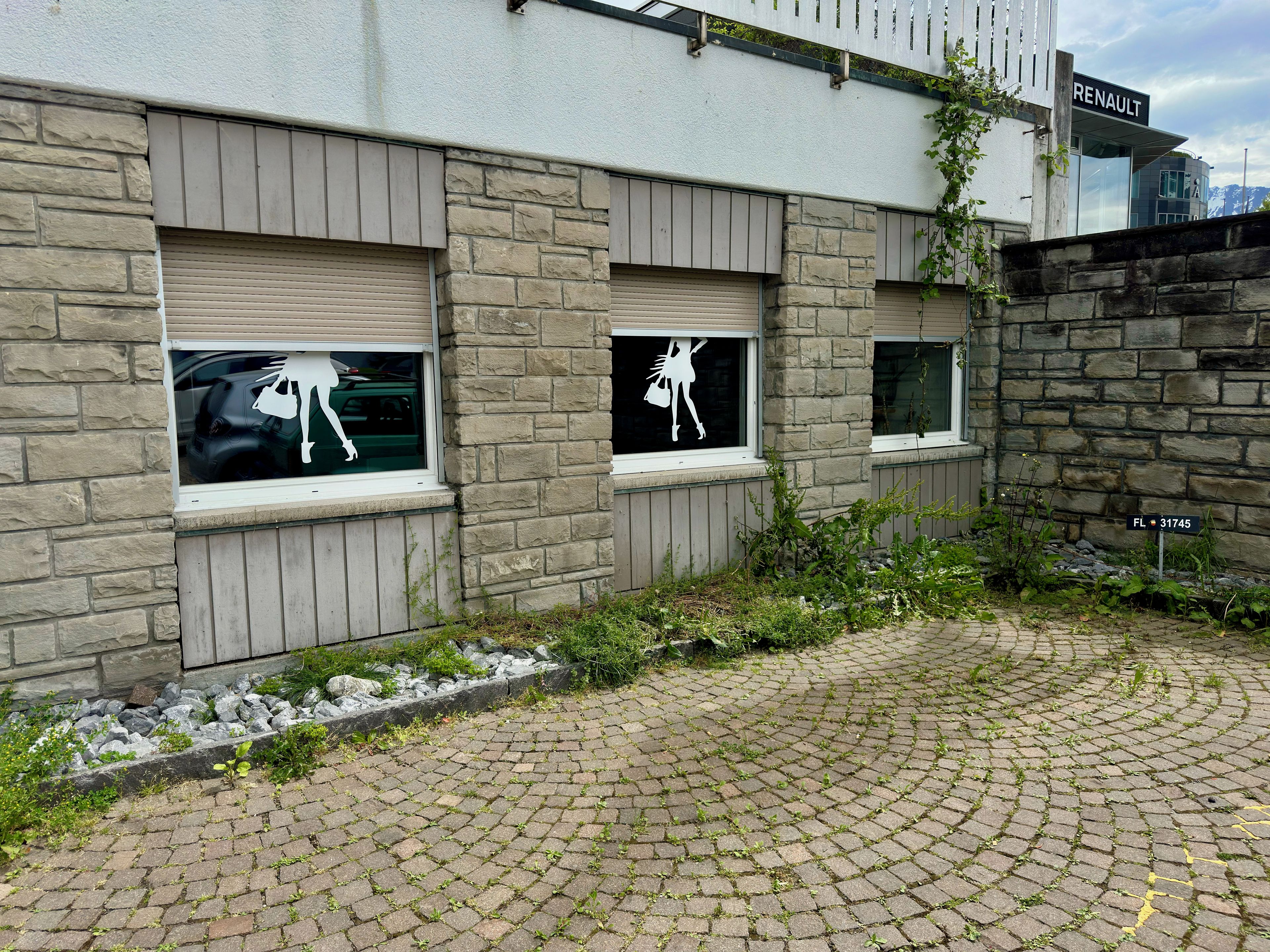Ein Gebäude mit steinverkleideter Fassade und Fenstern, in denen sich die Silhouetten einer Frau und eines Mannes abzeichnen.