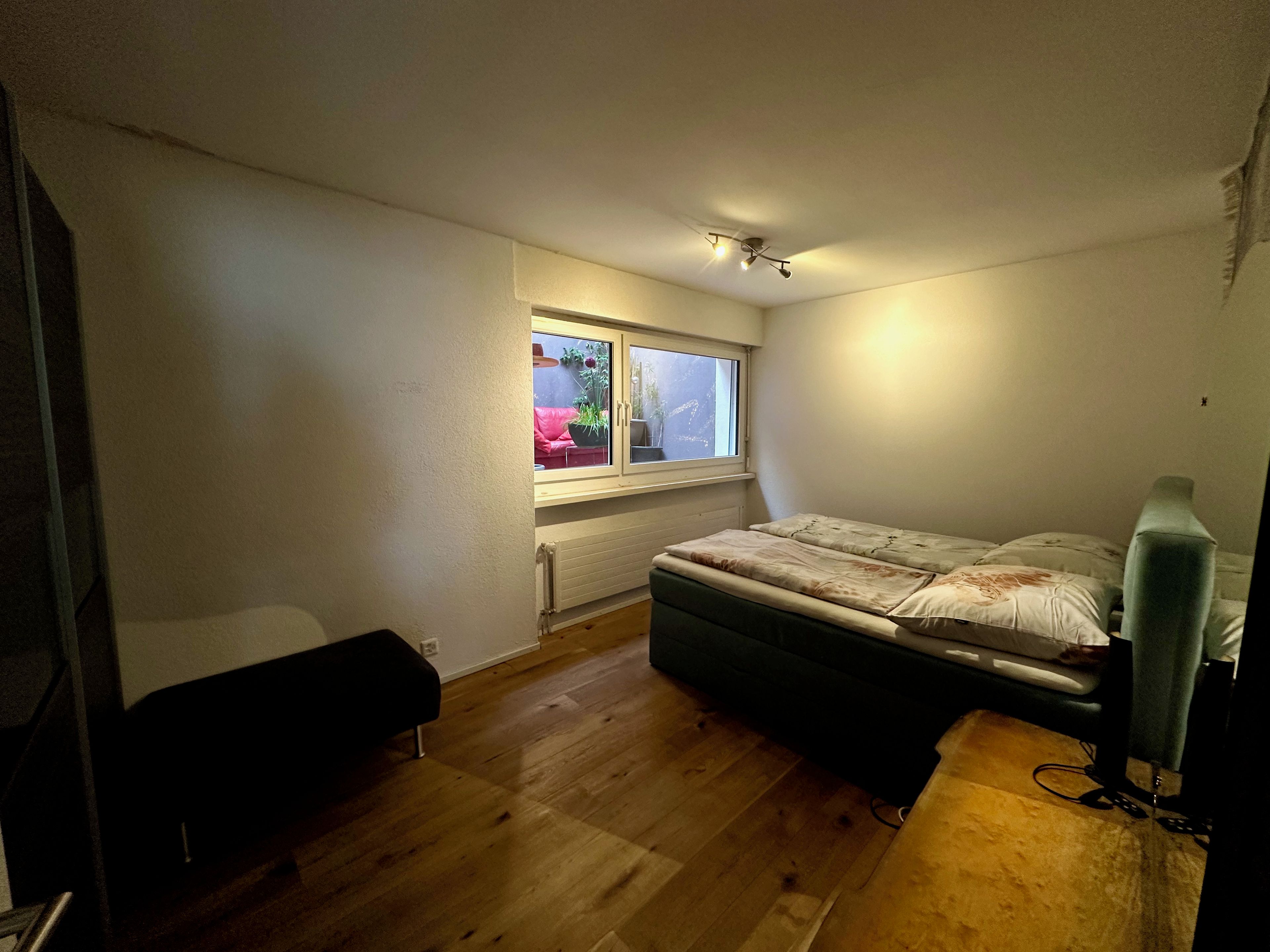 A small bedroom with a single bed, a window, a radiator, and a desk.