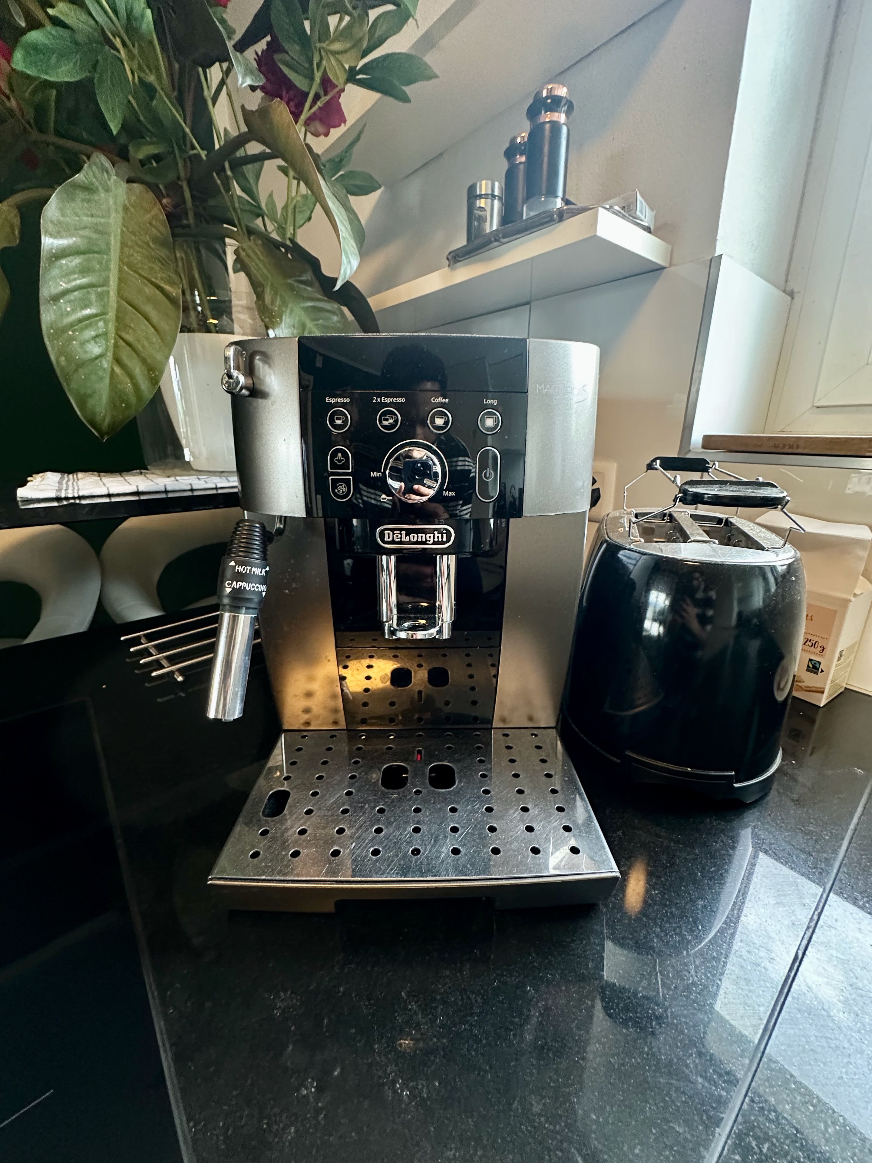Una cafetera con varias opciones de preparación, un hervidor y una planta al fondo.