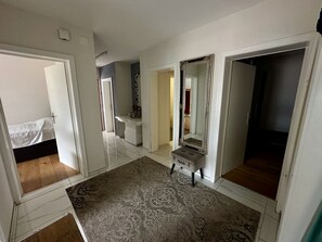 A hallway with a bed, a vanity with a mirror, and a patterned rug.