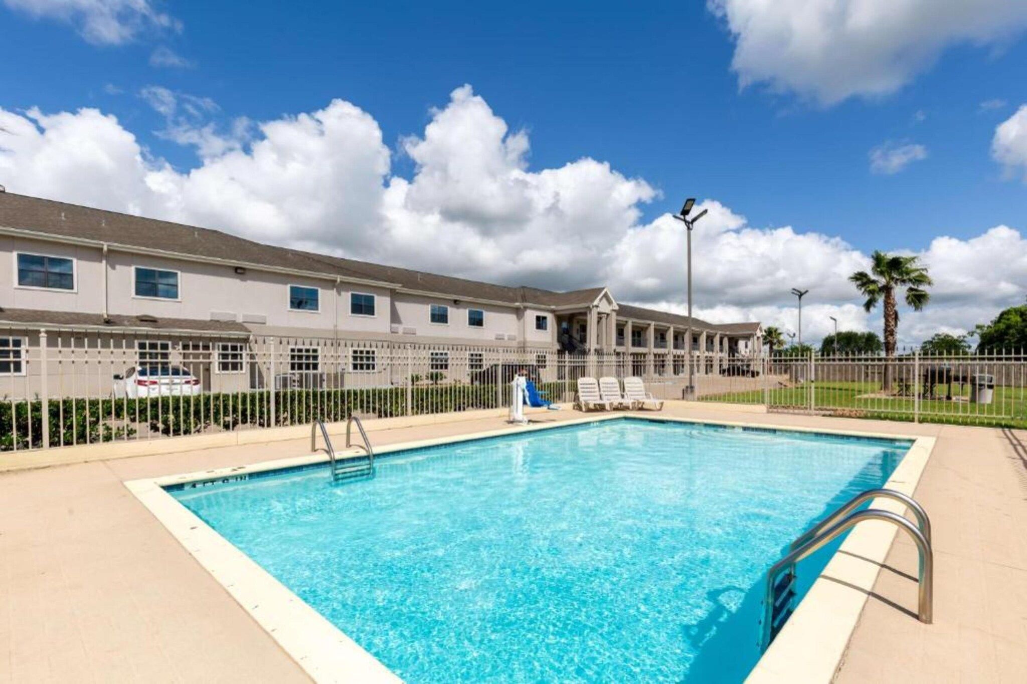 Una piscina con agua cristalina azul, rodeada por una valla, y un edificio con múltiples ventanas al fondo.