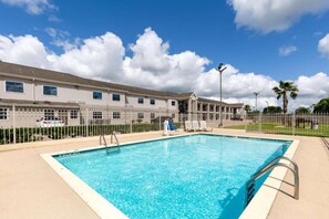 A swimming pool with a clear blue water, surrounded by a fence, and a building with multiple windows in the background. - 2 Queen Beds | Non-Smoking, Kitchen (Bay city TX)