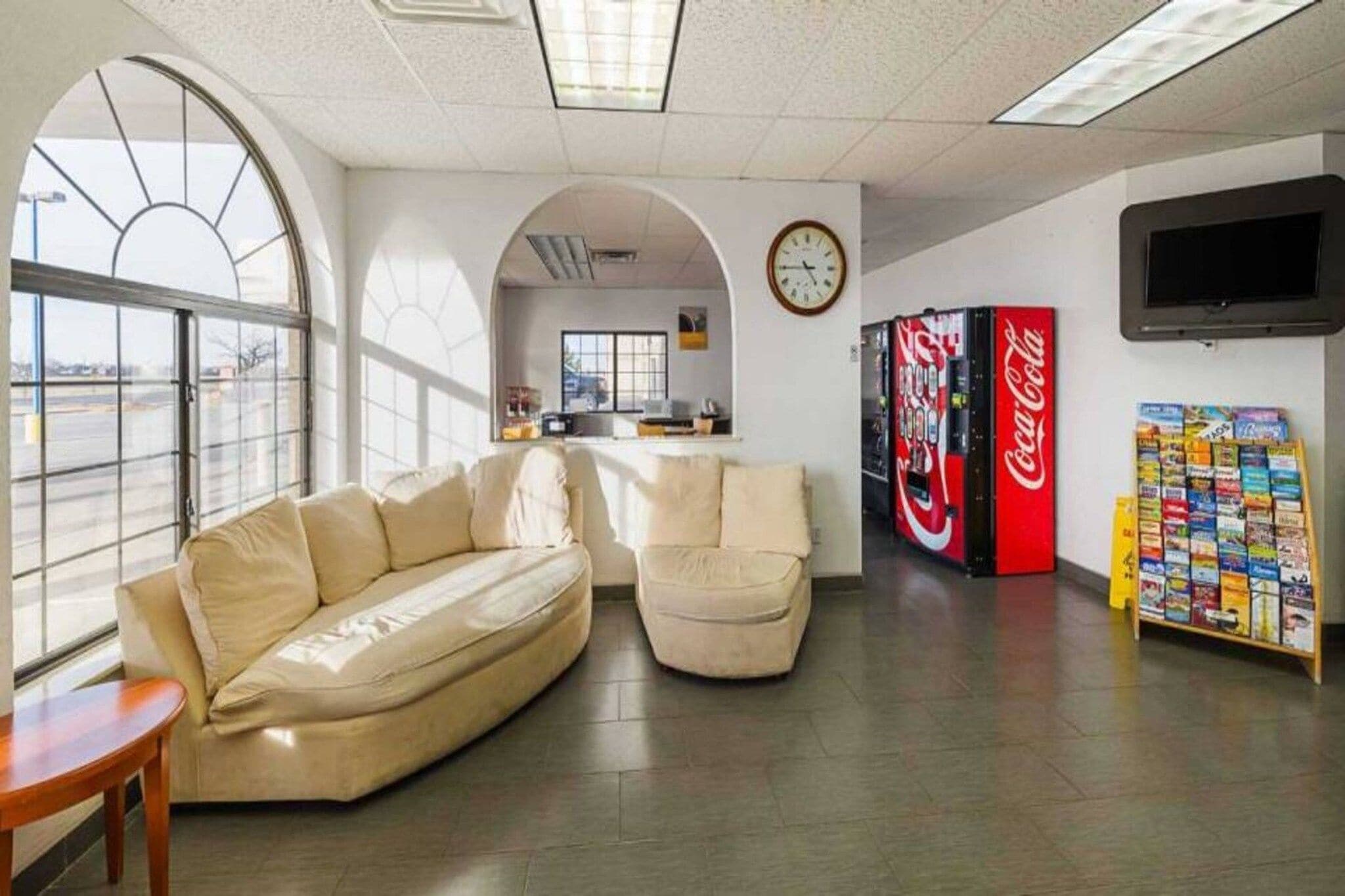 Een modern interieur met een bank, fauteuils, een klok, een Coca-Cola automaat en een tijdschriftenrek.
